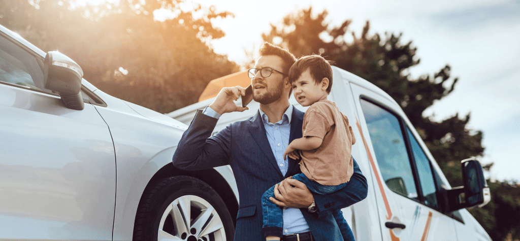 A man holds a small child while talking on the phone after a car accident