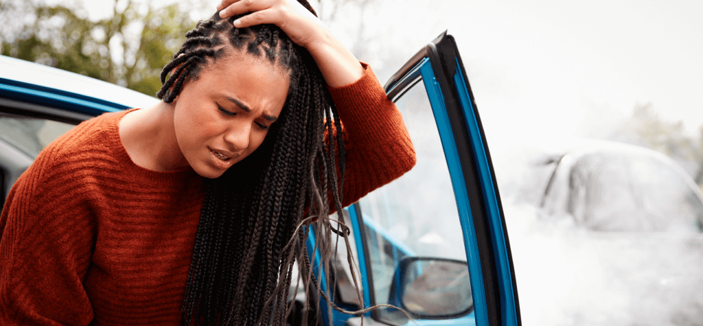 A person grips their head in pain while exiting a car