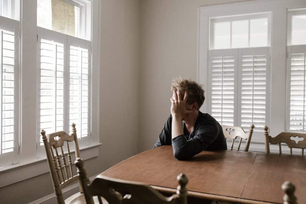 A man holds his head in his hands as he looks out the window