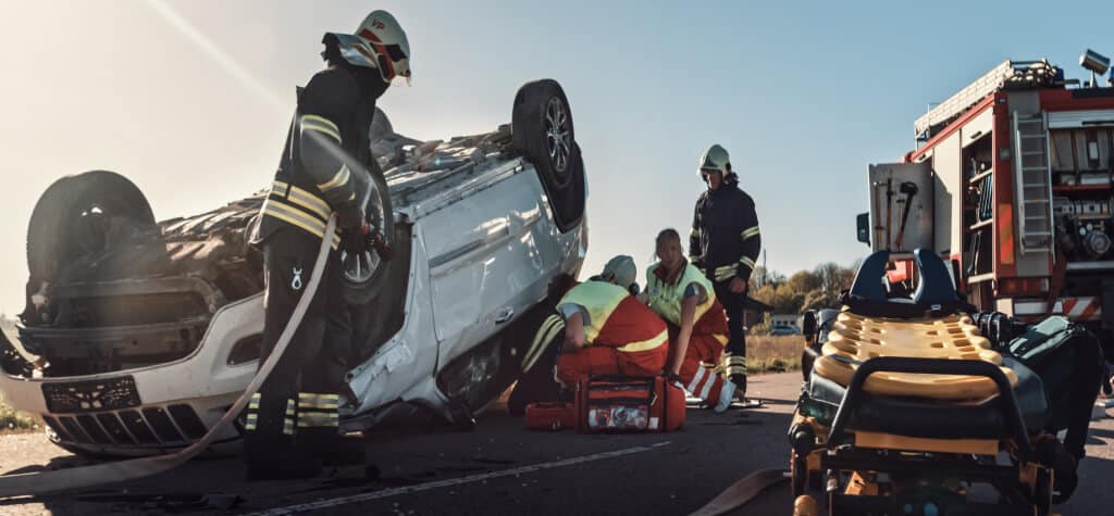 An overturned car surrounded by emergency personnel 