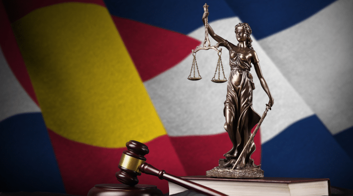 Justice Statue on book with gavel and Colorado state flag in background