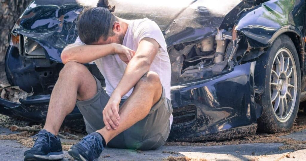 A distraught person sits in front of a totaled car
