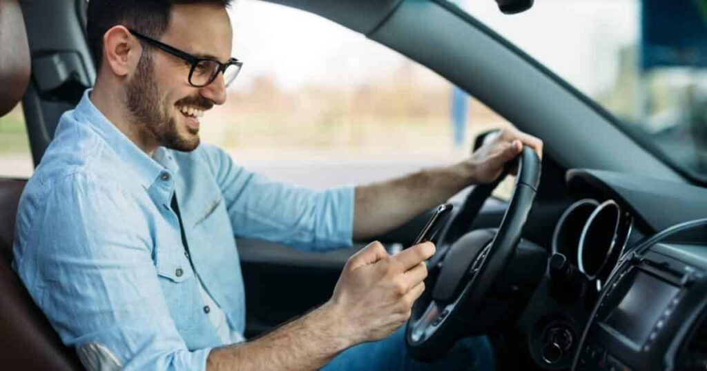A man grins while on his phone and driving
