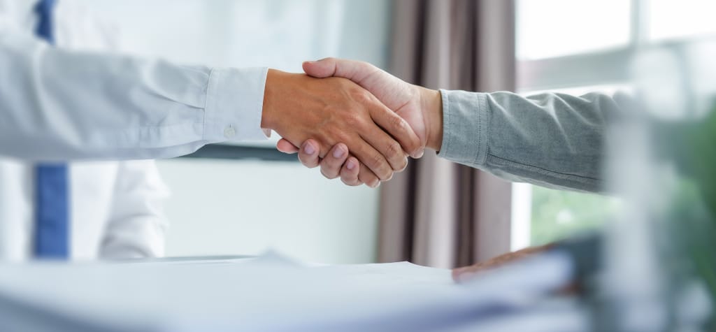 Two people shaking hands over a desk