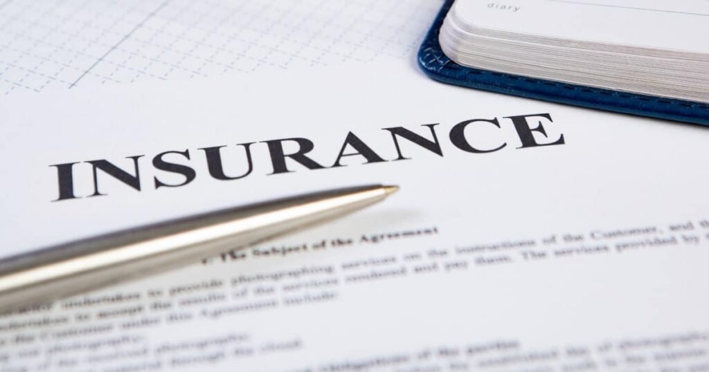 Insurance document with "INSURANCE" in bold, a silver pen on it, and a blue notebook in the background.