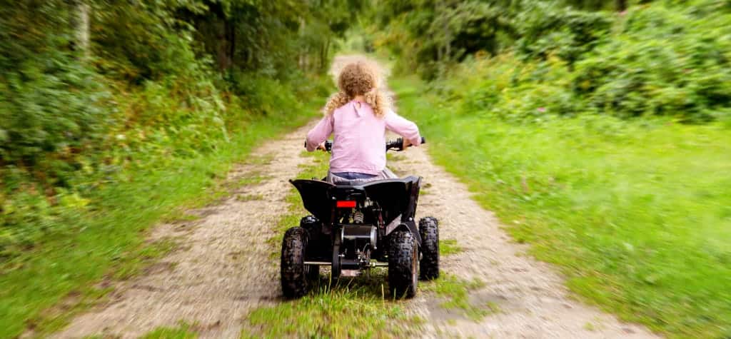 Child riding an ATV down a narrow, green forest trail