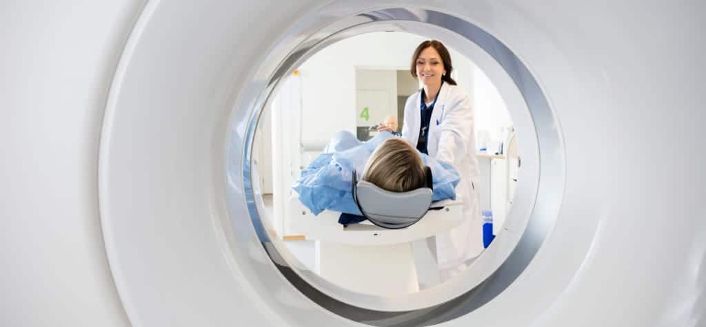 A patient lying inside an MRI machine, with a smiling healthcare professional standing nearby.